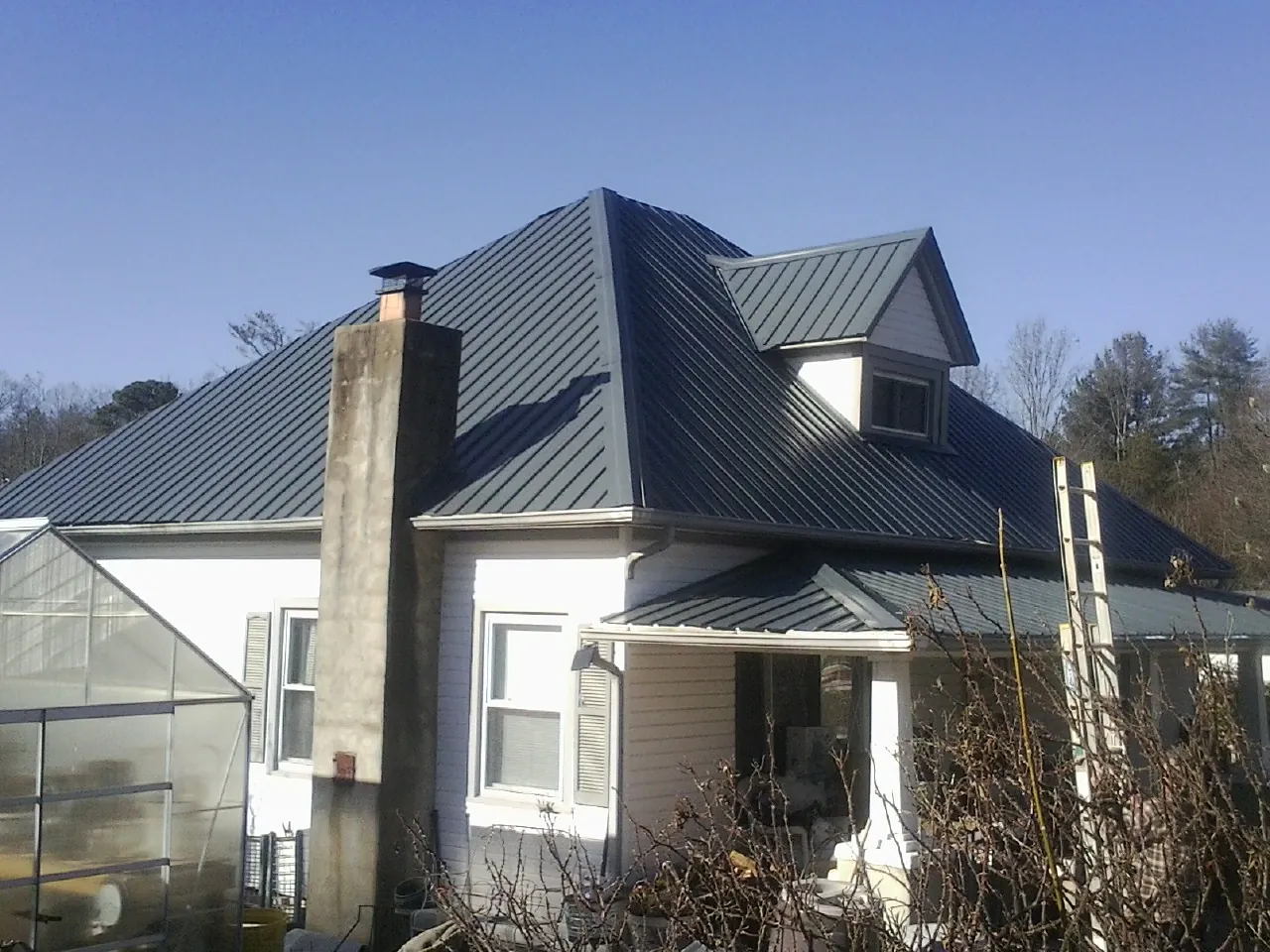 Dark blue standing seam metal roof on a white farmhouse with dormer — Slate & Tile Roof Repair by Roofing Brothers in Swisshome