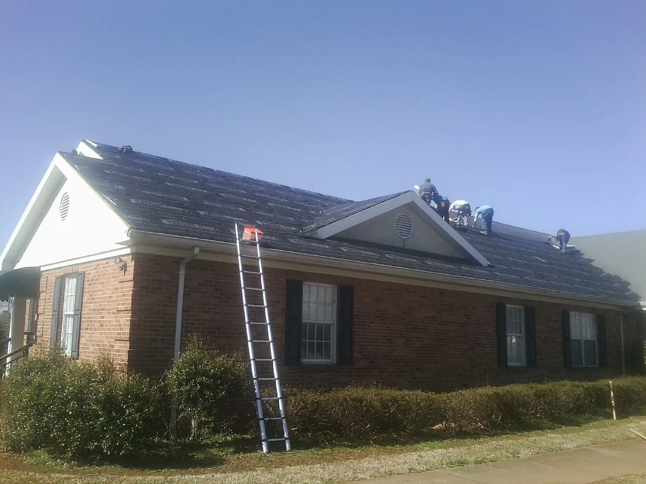 Crew tearing shingles off a brick ranch roof with a ladder set — Metal Roof Repair work by our crew in Swisshome