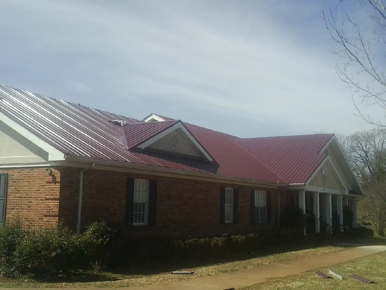 Red metal roof with gabled entries on a long brick building, from a Hail Damage Roof Repair job in Swisshome