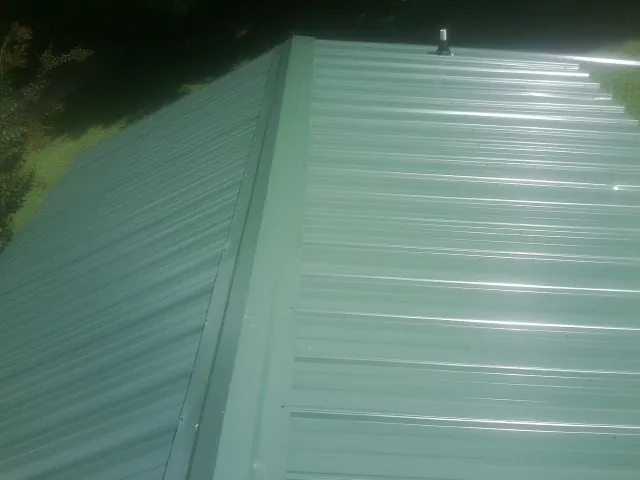 New green metal panels meeting at the ridge of a roof — Flat Roof Repair work by our crew in Swisshome