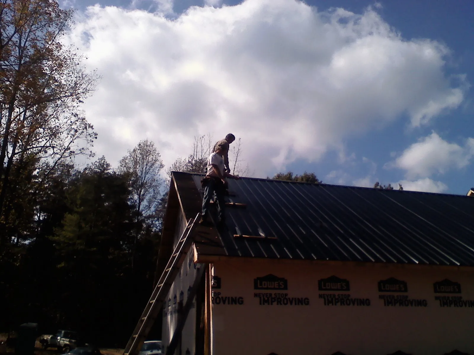 Roofer fastening dark metal panels high against a cloudy sky, from a Roof Inspection job in Swisshome