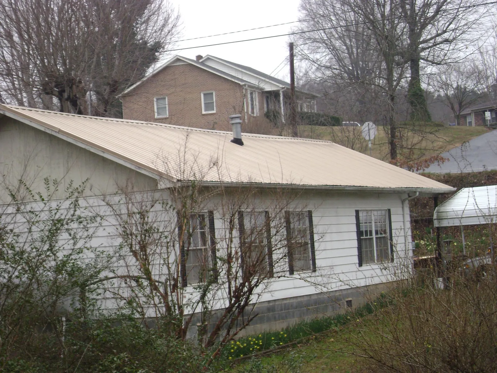 Tan metal roof on a white sided house set into a hillside — Commercial Roofing by Roofing Brothers in Swisshome