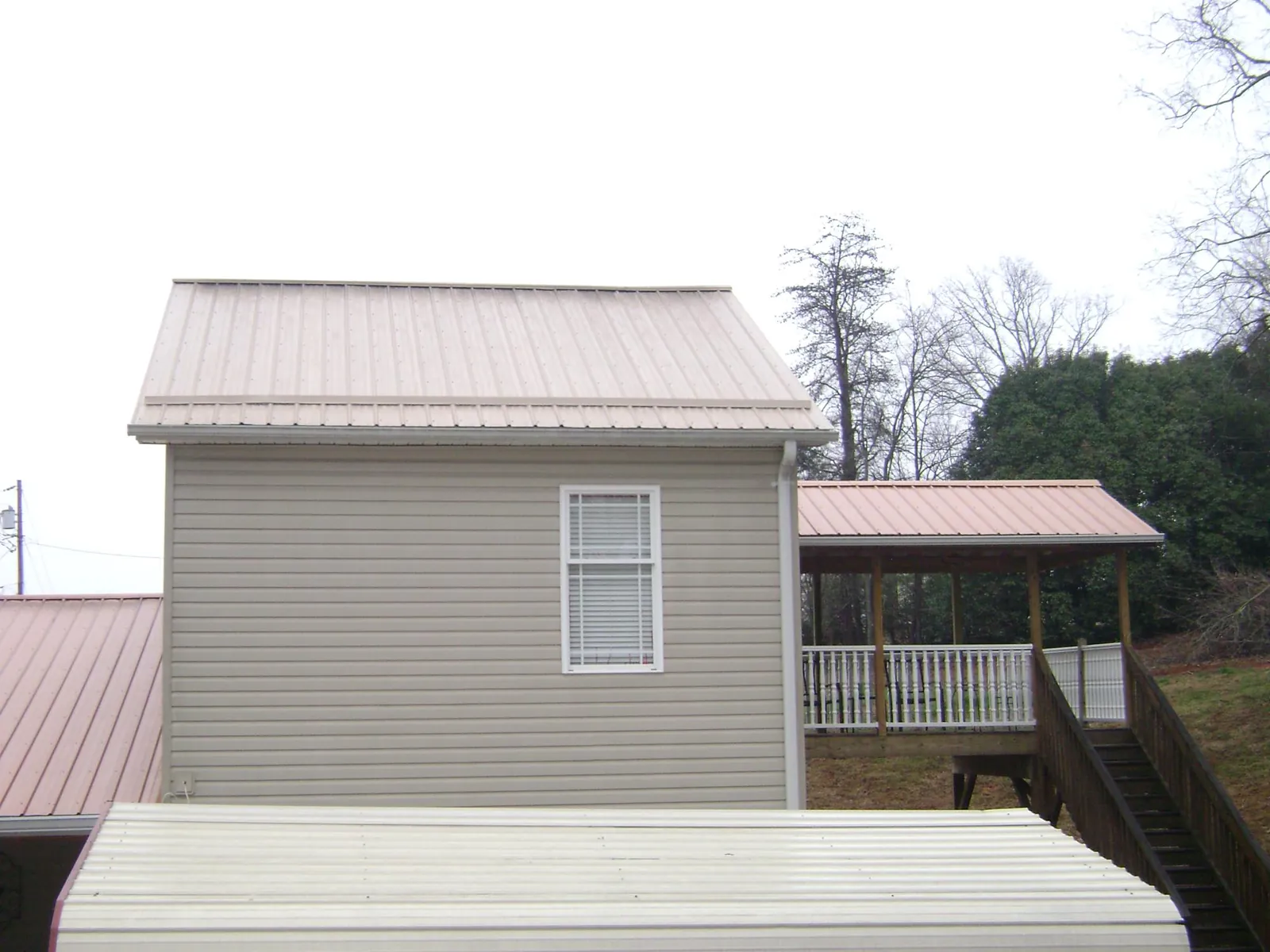 Tan metal roofs on a two story addition and attached porch, from a Roof Replacement job in Swisshome